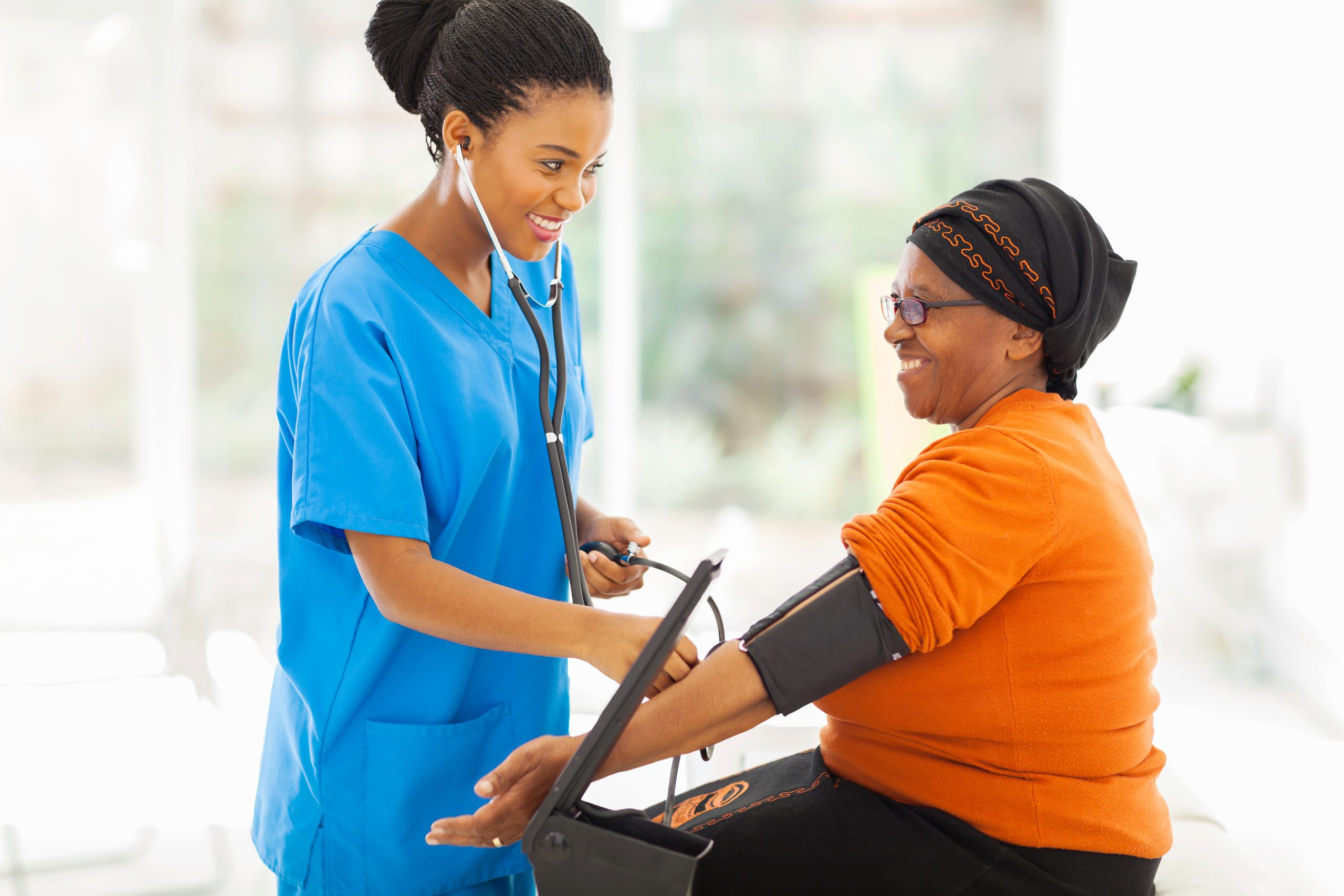 smiling african nurse checking senior patient's blood pressure